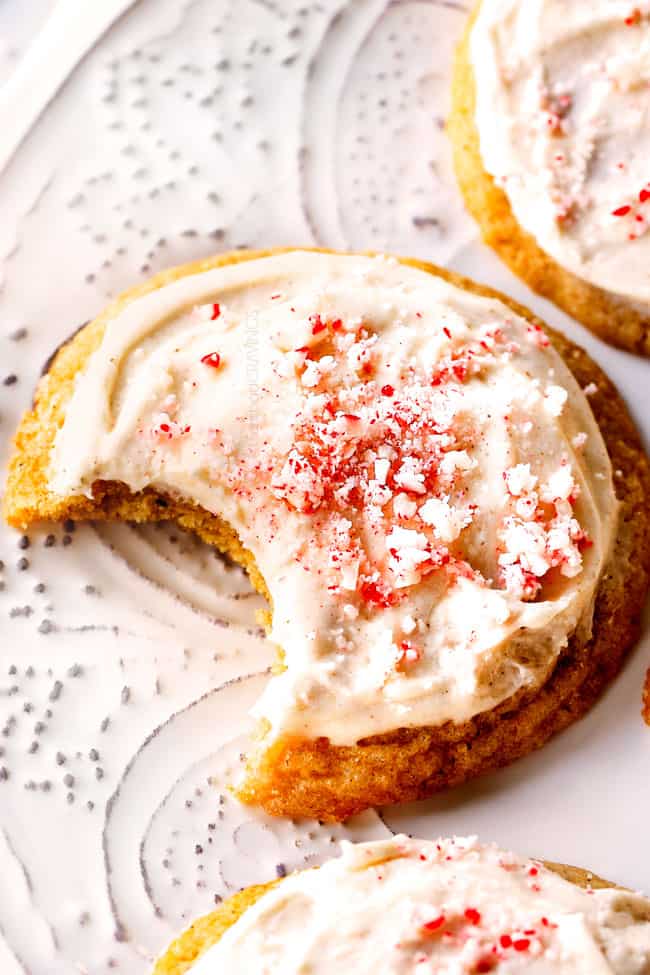 close up of an eggnog cookie topped with eggnog frosted and crushed candy canes. A bite is missing. 