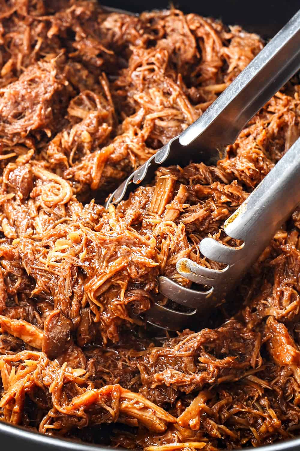 showing how to serve BBQ Pulled Pork recipe by picking up the shredded pork with tongs