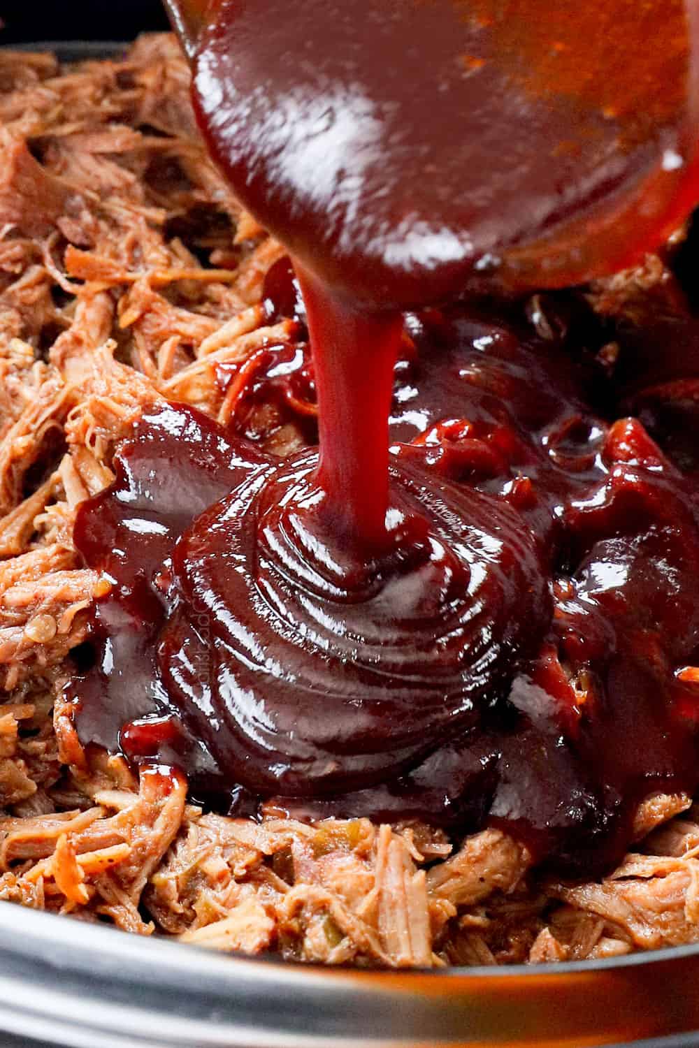 showing how to make pulled pork recipe by pouring barbecue sauce over the pulled pork and stirring to combine