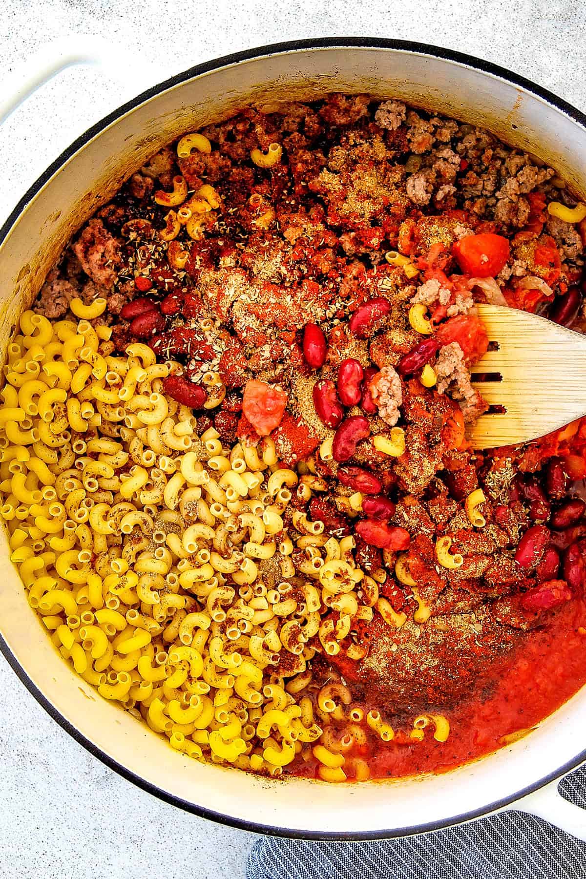 top view showing ingredients for chili mac:  ground beef, macaroni, kidney beans, crushed tomatoes, diced tomatoes, seasonings