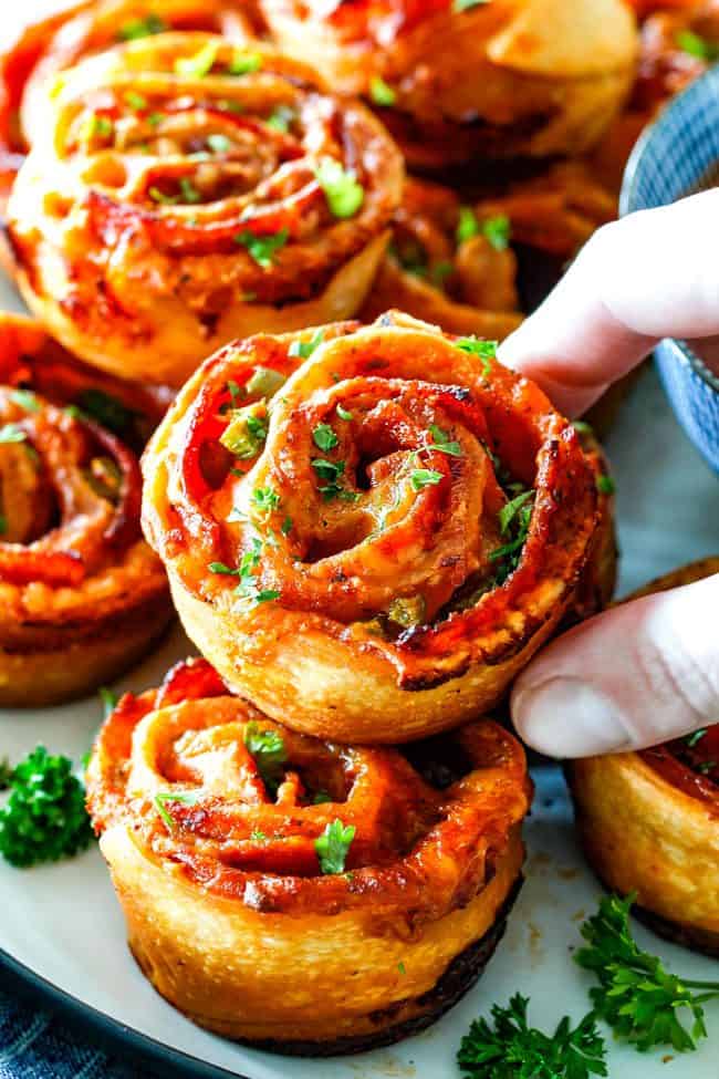 grabbing a cooked pizza pinwheel from a platter of pizza pinwheels