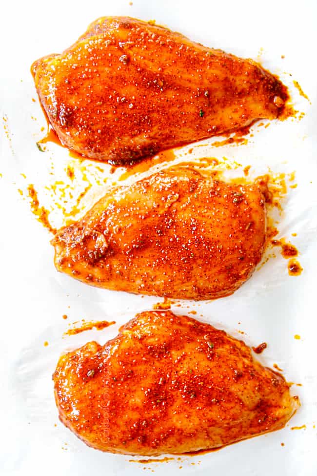 showing how  to make Chili Lime Chicken by slathering 3 chicken breasts on parchment paper  with the wet rub on pa