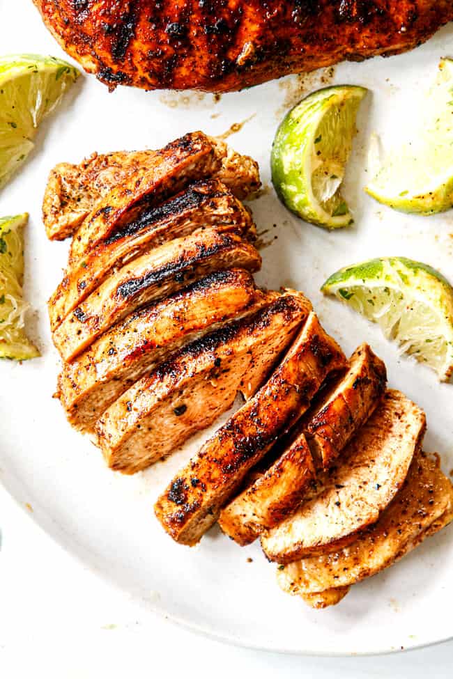 top view of showing  how to make  chili lime chicken by thinly slicing on  a white plate  and squeezing with lime wedges