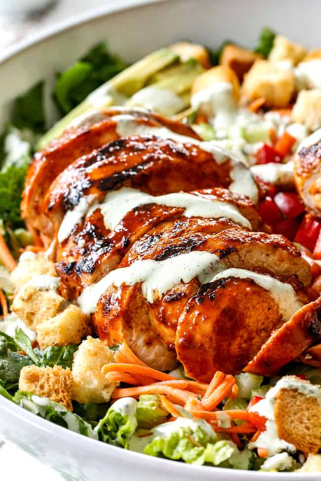 up close of sliced Buffalo Chicken in Buffalo Chicken Salad in a white bowl with blue cheese, celery, carrots, avocado, red bell peppers and lettuce
