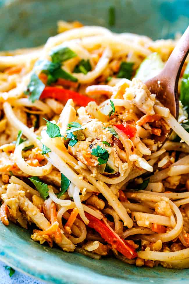 Close up view of a fork taking a bite of Chicken Pad Thai.