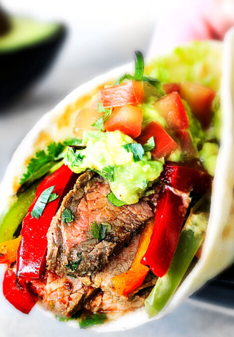 up close showing how to serve steak fajitas by wrapping up with steak, bell peppers, guacamole and pico de gallo