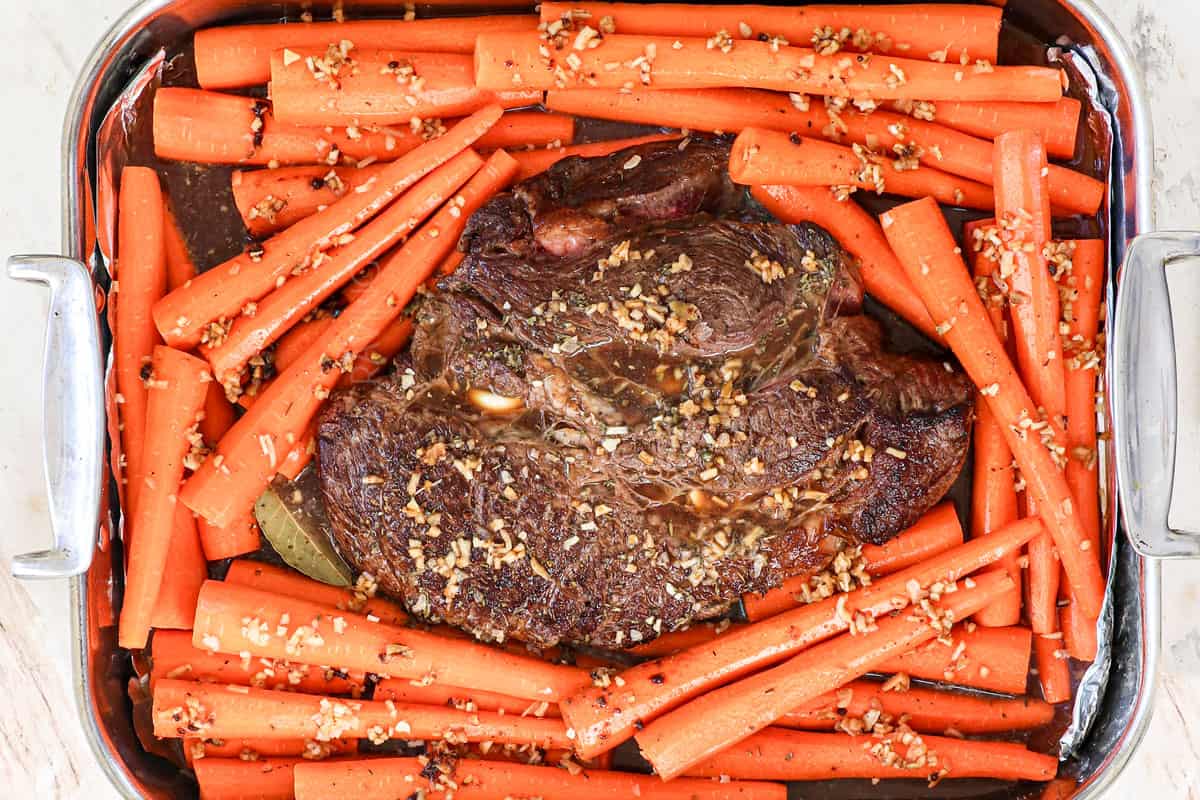 showing how to cook a roast in the oven by baking in a large pan until tender with carrots