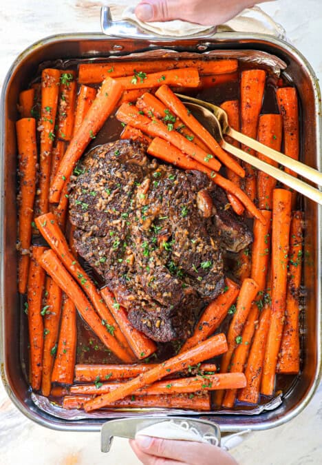 holding the roast in a pan surrounded by carrots that's just come out of the oven