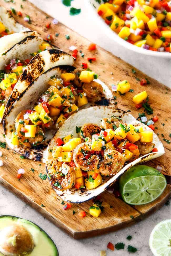 Cilantro Lime Shrimp Tacos with Mango Salsa and Avocado lined in a row on a brown cutting board