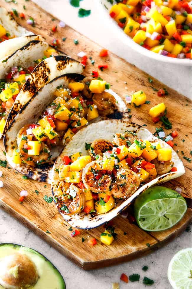 best Shrimp Tacos with Mango Salsa and Avocado lined in a row on a brown cutting board