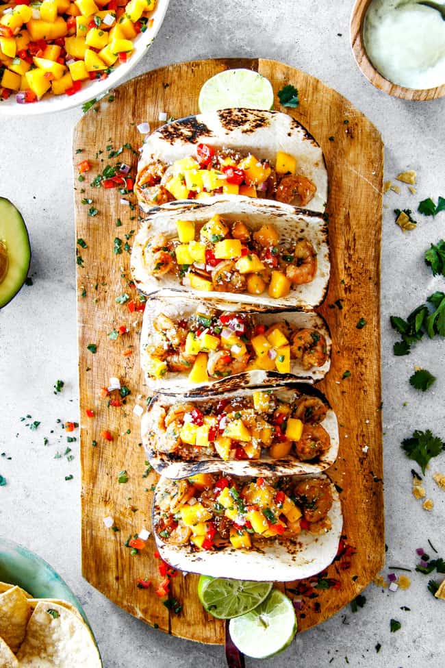 easy Shrimp Tacos with Mango Salsa and Avocado lined in a row on a brown cutting board