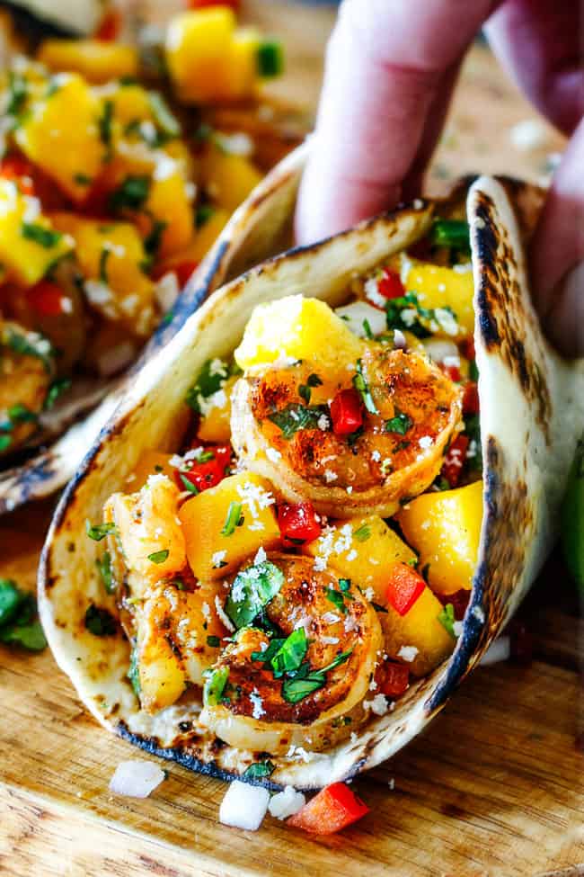 up close of Shrimp Tacos with Mango Salsa and Avocado being grabbed by a hand to eat