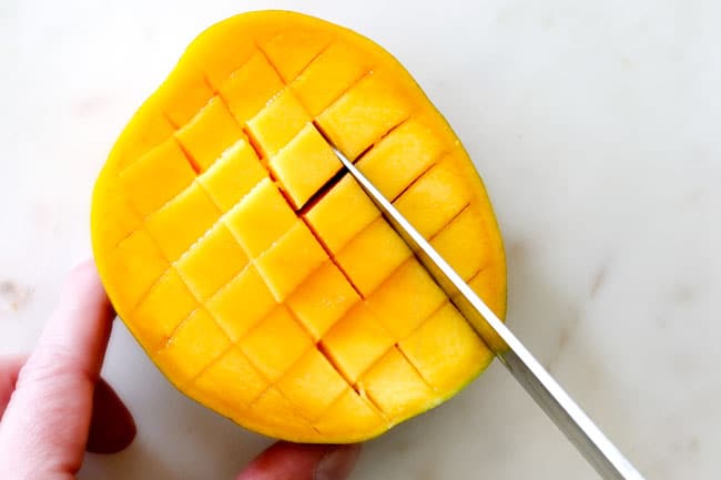 How to Cut A Mango showing cutting a grid pattern in mango flesh on a white cutting board