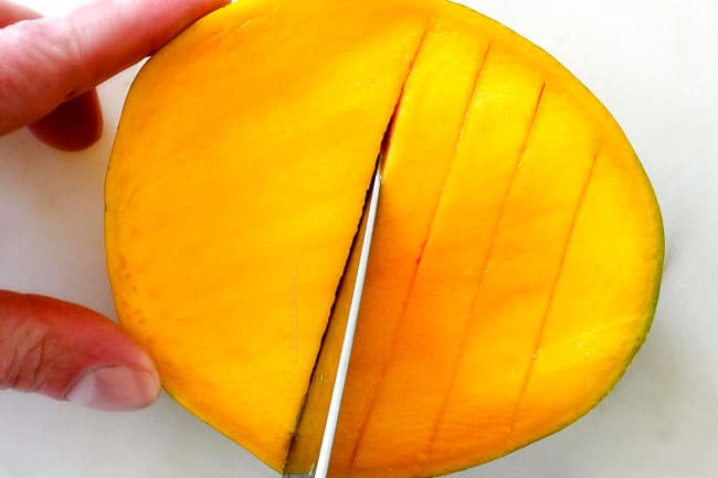 How to Cut A Mango showing slicing mango into vertical slices on a white cutting board