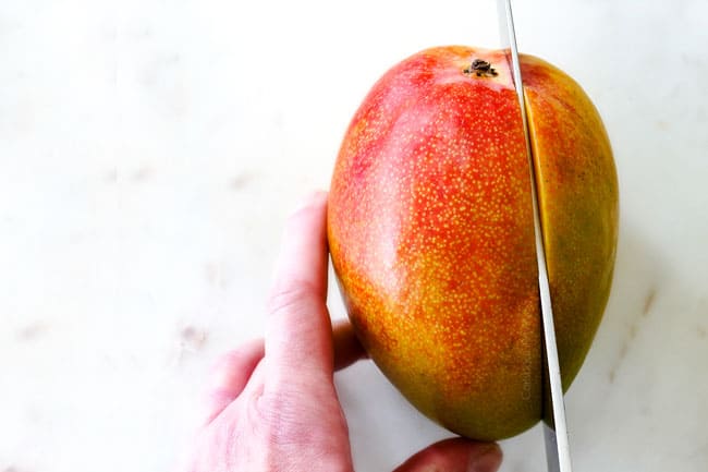 How to Cut A Mango showing locating stem to cut around it on a white cutting board