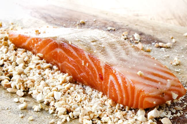 showing how to make Honey Soy Salmon by brushing salmon by pressing cashews into salmon on a cutting board