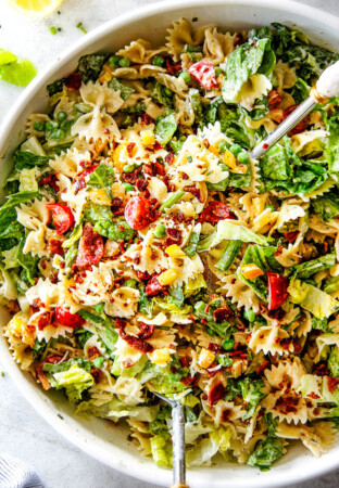 Top Shot of Best BLT Pasta Salad in a white bowl with white tongs lifting the salad up
