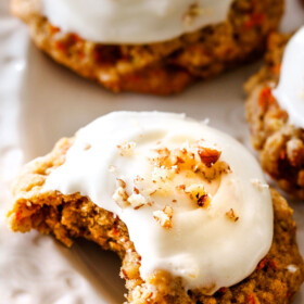 Up close of soft Carrot Cake Cookies with Cream Cheese Frosting with a bite taken out of it on a white plate