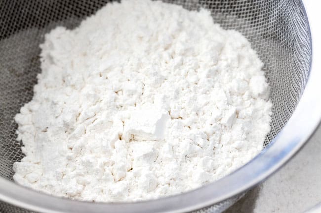 How to make easy Coconut Cake by sifting cake flour into sugar in a large bowl