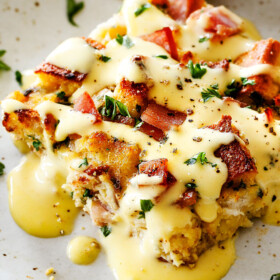 Eggs Benedict Casserole on a speckled plate being smothered by Hollandaise Sauce