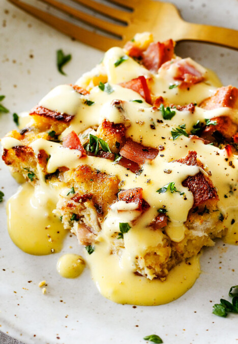 Eggs Benedict Casserole on a speckled plate being smothered by Hollandaise Sauce