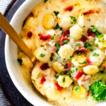top view of white bowl England Clam Chowder with a spoon with potatoes, bacon, onions, celery and garlic