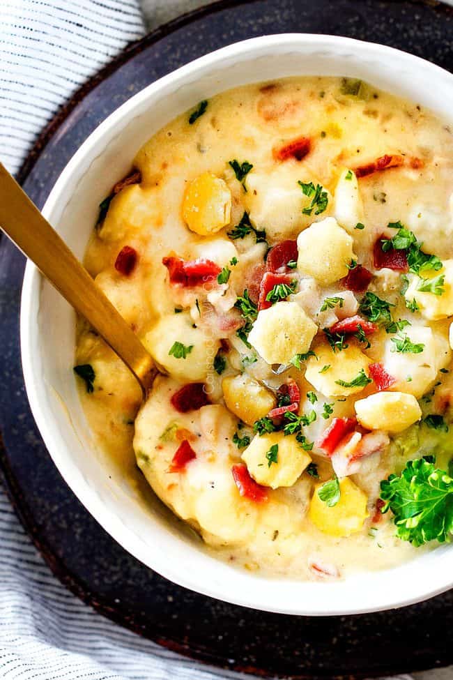 top view of white bowl England Clam Chowder with a spoon with potatoes, bacon, onions, celery and garlic