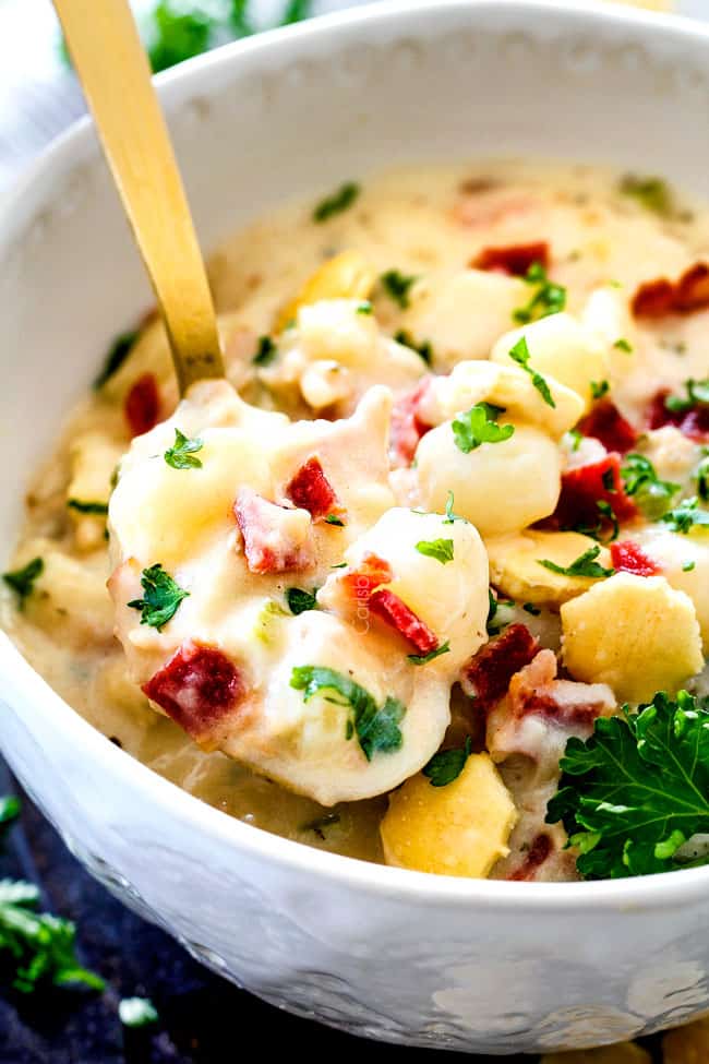 white bowl thick New England Clam Chowder with a spoon with potatoes, bacon, onions, celery and garlic