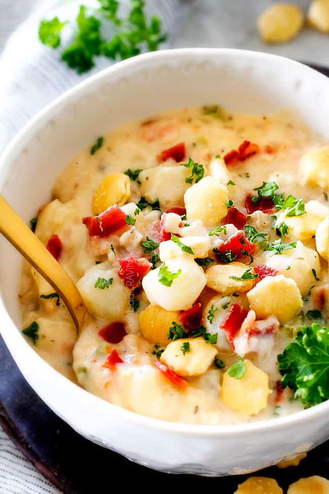 white bowl easy New England Clam Chowder with a spoon with potatoes, bacon, onions, celery and garlic