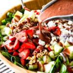 Pouring Balsamic dressing on strawberry salad in wooden bowl