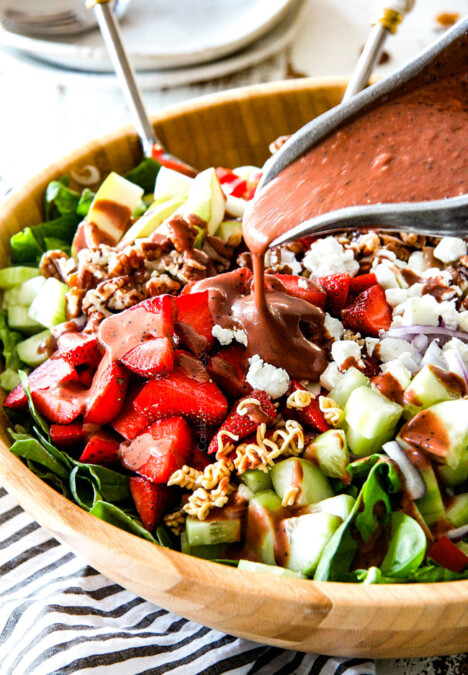 Pouring Balsamic dressing on strawberry salad in wooden bowl