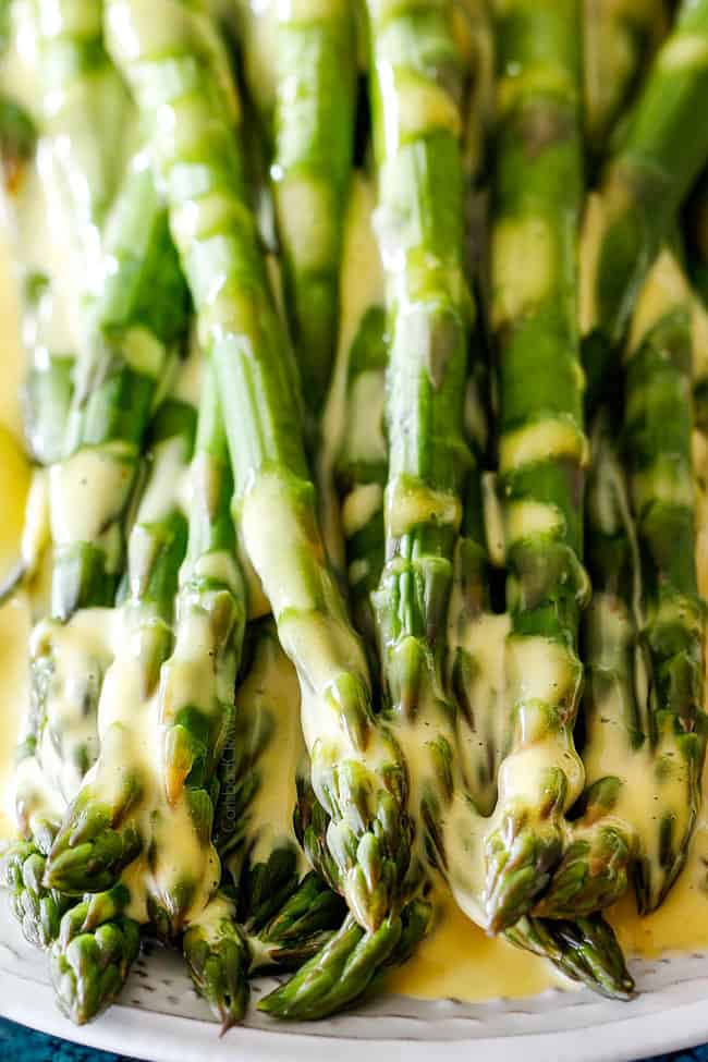 Up close of asparagus on a white platter that has been drizzled with Blender Hollandaise Sauce