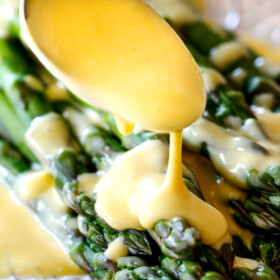 Spooning rich and creamy Blender Hollandaise Sauce on asparagus on a white platter