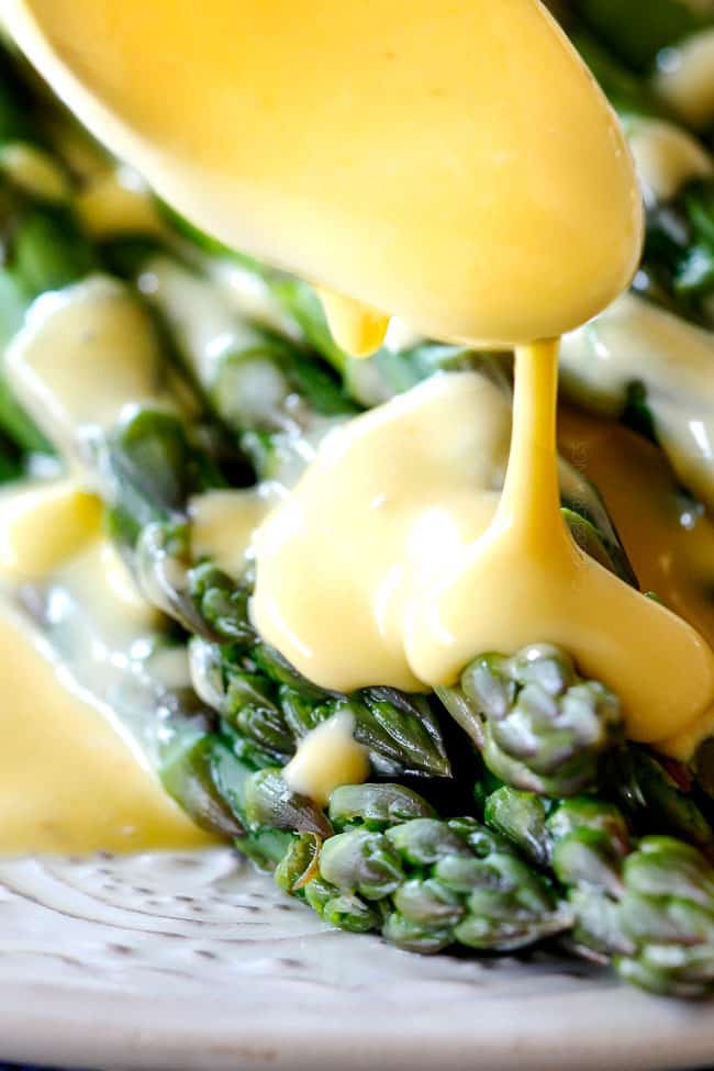 Spooning rich and creamy Blender Hollandaise Sauce on asparagus on a white platter