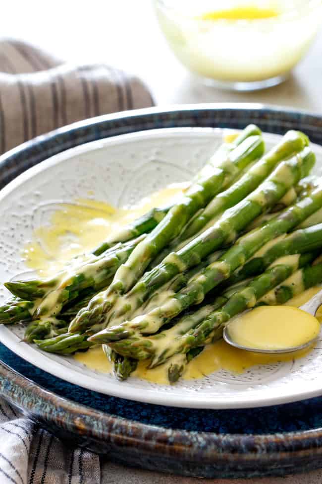 langt væk skud af asparges på et hvidt fad, der er dryppet med easy Blender Hollandaise Sauce