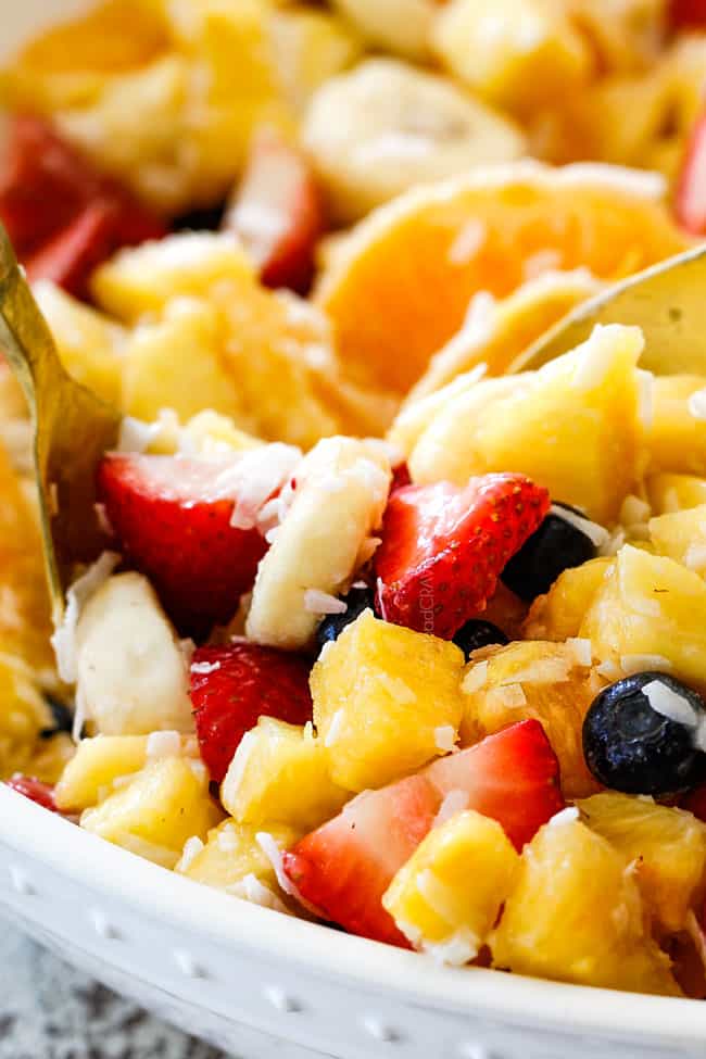 up close view of easy Pina Colada Fruit Salad with pineapple, coconut, mandarin oranges, strawberries and blueberries in a white bowl