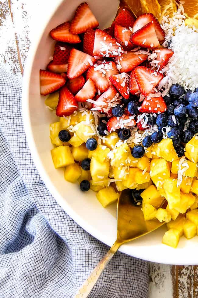 up close top shot of best Pina Colada Fruit Salad with pineapple, coconut, mandarin oranges, strawberries and blueberries in a white bowl