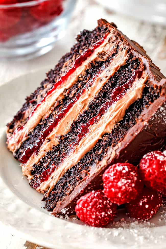 up close of a slice of moist Chocolate Raspberry Cake on its side showing layers of dark chocolate cake, raspberry jam filling, chocolate ganache and chocolate mousse