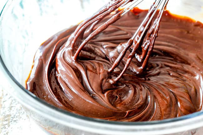 showing how to make chocolate mousse cake by whisking ganache in a glass bowl until smooth