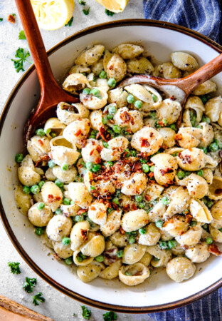 Top view of Creamy Pasta Salad with Peas and Bacon with a wood serving spoon