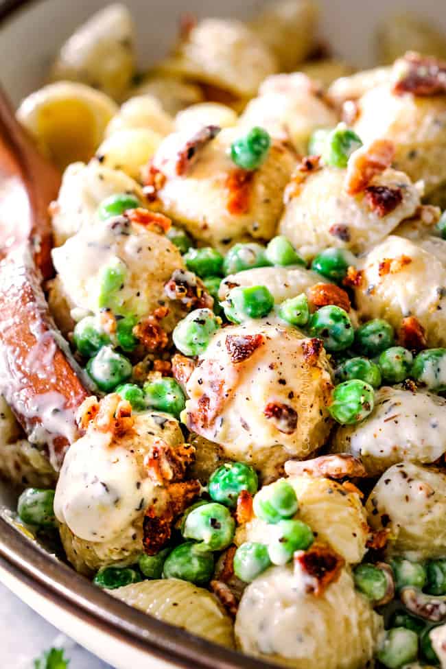 up close view of creamy pasta salad with macaroni, bacon and peas in a white bowl