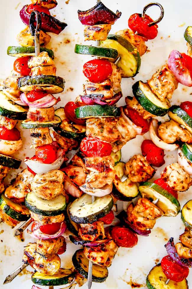 easy chicken souvlaki skeweres on a white platter with tomatoees and zucchini