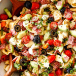 top view of easy Italian Pasta Salad with pepperoni, tomatoes, olives, cucumbers, mozzarella with wooden tongs