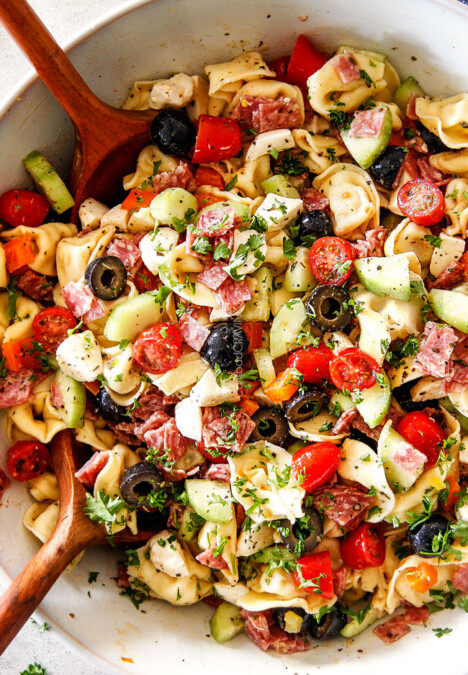 top view of easy Italian Pasta Salad with pepperoni, tomatoes, olives, cucumbers, mozzarella with wooden tongs