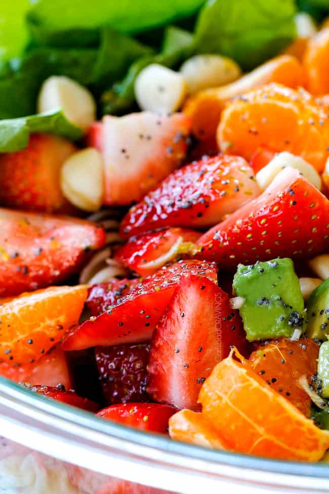 up close of strawberries, avocados, mandarin oranges in a glass bowl with poppy seed dressing
