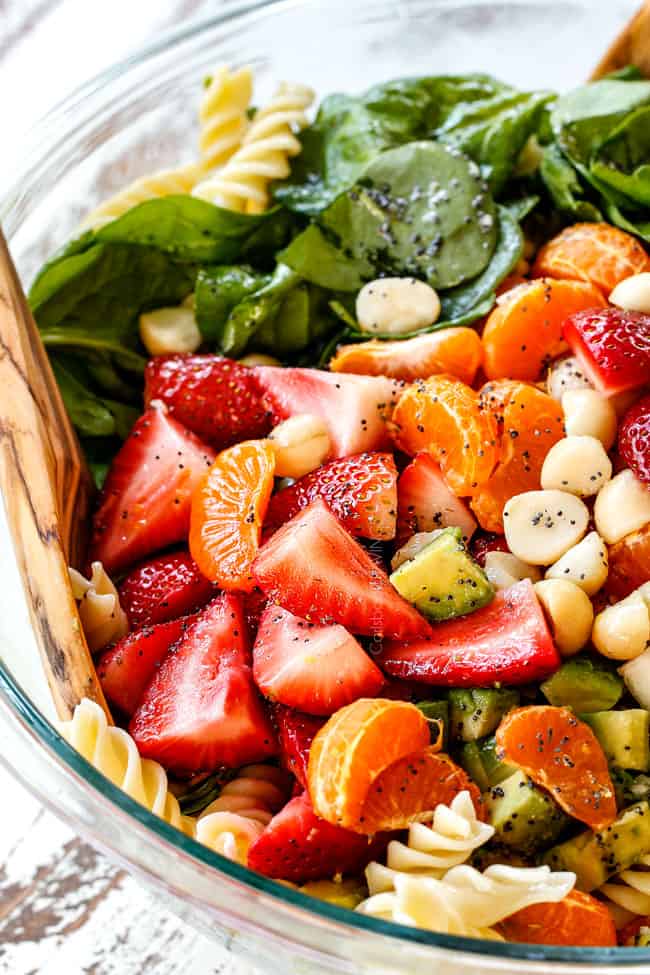 Mixing pasta, strawberries, spinach, Mandarin oranges, avocados, macadamia nuts and past in a glass bowl for pasta salad