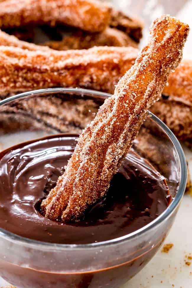 one churro dipping in dark chocolate sauce in a glass bowl