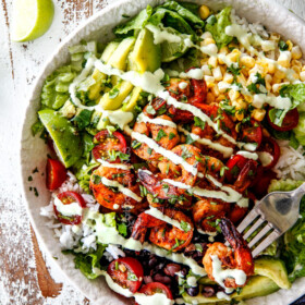 top view of shrimp Burrito Bowl with chipotle shrimp, tomatoes, avocados, corn, black beans and rice drizzled with cilantro lime dressing