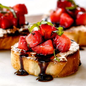 side view of best Strawberry Goat Cheese Bruschetta on a white cutting board with Balsamic Reduction