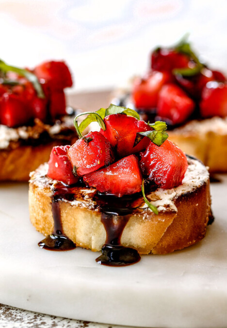 side view of best Strawberry Goat Cheese Bruschetta on a white cutting board with Balsamic Reduction